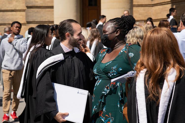 A man and a woman smile happily at each other in a crowd of graduates and family outside Convocation Hall.