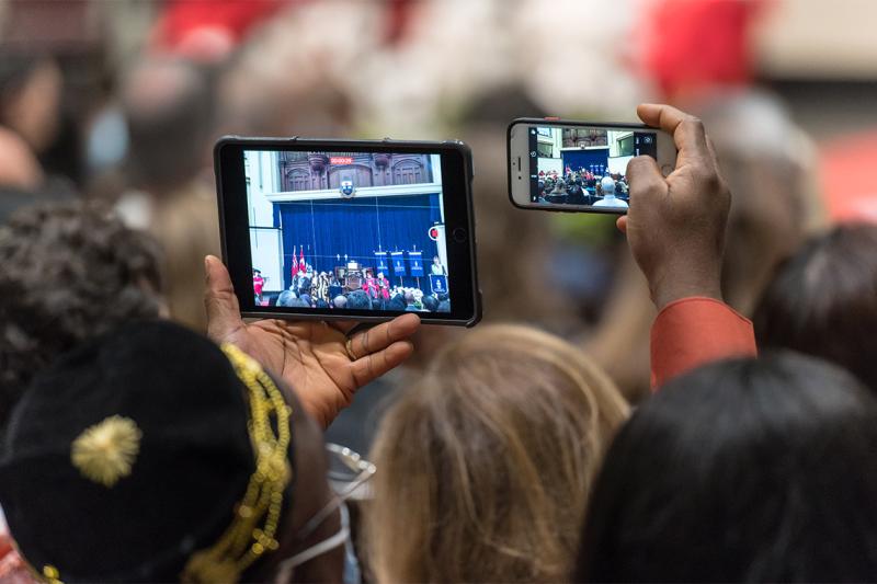 People in an audience hold up phones to film the Convocation Hall stage.