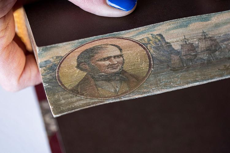 Hands fan out a book's pages to reveal a hidden image of a man with a Victorian haircut.