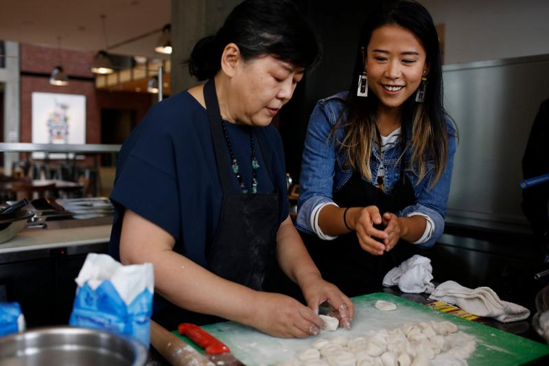 Ningsha Zhong shapes dumplings at a kitchen counter as her daughter Domee Shi smiles.