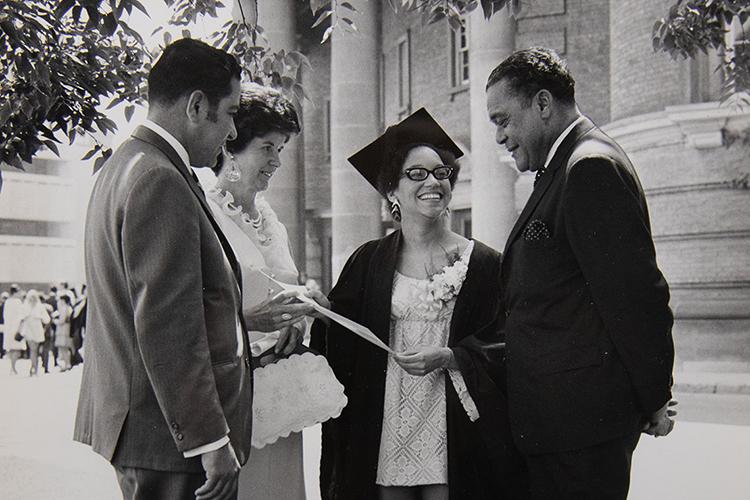 Aston Foreman smiles down at the paper that Eleanor Phillips is holding. She is wearing academic robes.