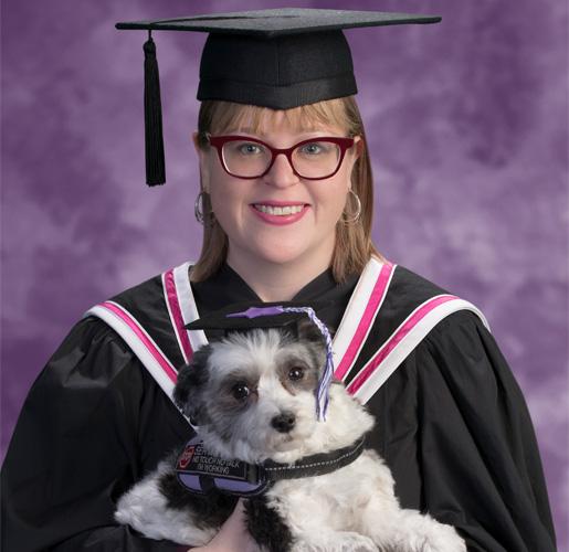 Emily Wright wears her academic mortarboard and holds her service dog Kailey, who is also wearing a tiny mortarboard.