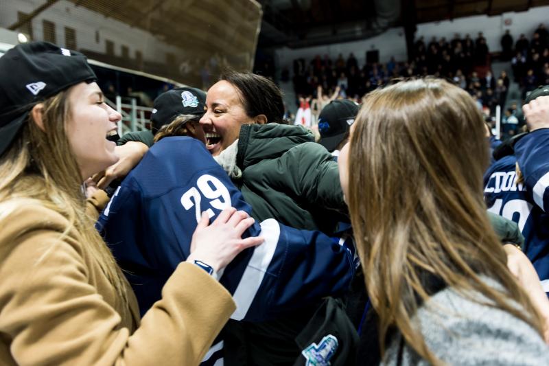 Safiya Muharuma and Madeline Albert hug excitedly in a crowd at a hockey game.