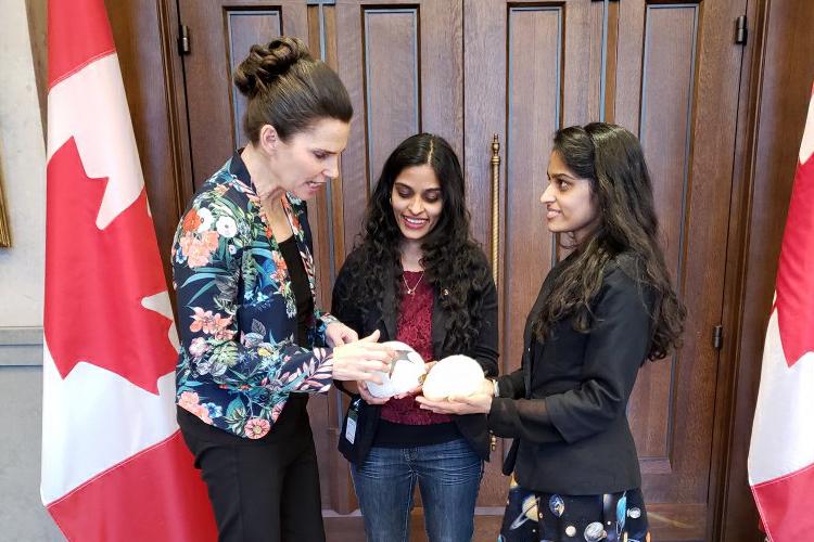 Standing between two Canadian flags, Kirsty Duncan looks at the model brains being held by Swapna and Sandhya Mylabathula  (photo courtesy of Sandhya Mylabathula)