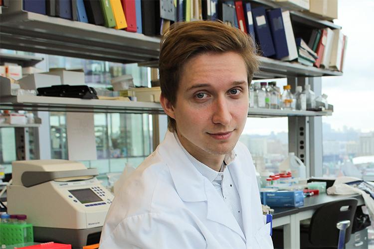 Daniel Szulc looks over his shoulder in a busy office with shelves lined with books and glass sample bottles.