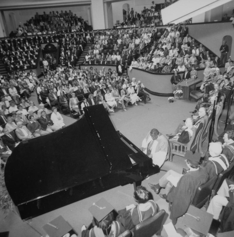 A grand piano fills the floor at Convocation Hall. Oscar Peterson, in robes, is playing while a packed house listens.