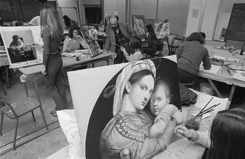 A student paints a Madonna and Child on an easel. Behind her, other students paint copies of great artworks.