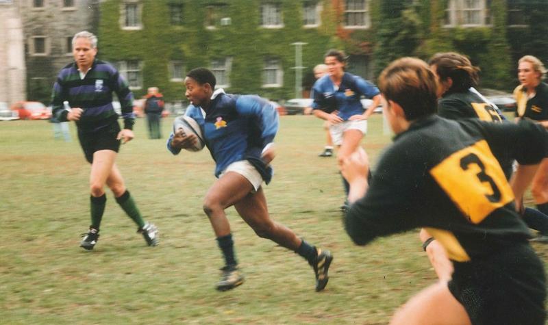 Marlene Donaldson runs across back campus, holding a rugby ball, as other players race to catch up.