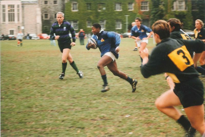 Marlene Donaldson runs across back campus, holding a rugby ball, as other players race to catch up.