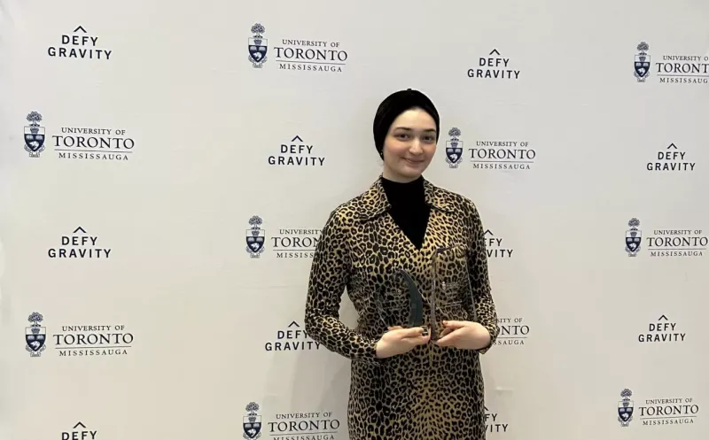 Mariam holding two awards and wearing a leopard-print coat