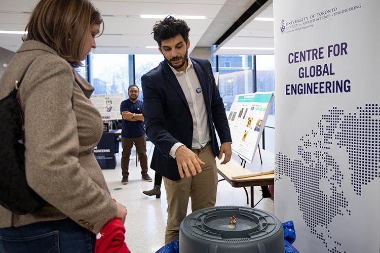 A student from the Centre for Global Engineering points at a gray plastic device while a woman looks on