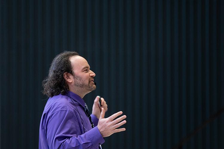 Jeffrey Rosenthal gestures animatedly while speaking in front of a curtained backdrop