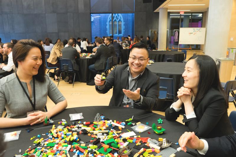 Choi sitting at a table covered in Lego bricks with two others