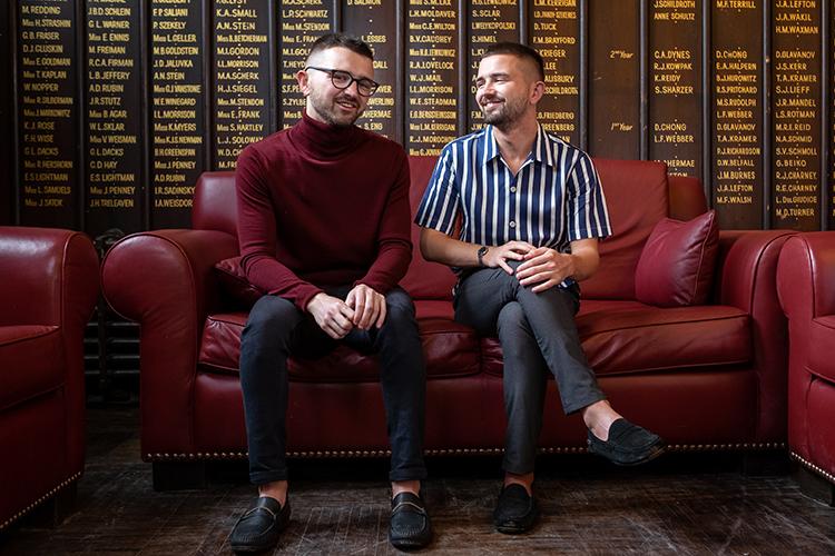 Patrick and Curtis Sobchak sitting on a large sofa in front of a wall carved with the names of U of T graduates