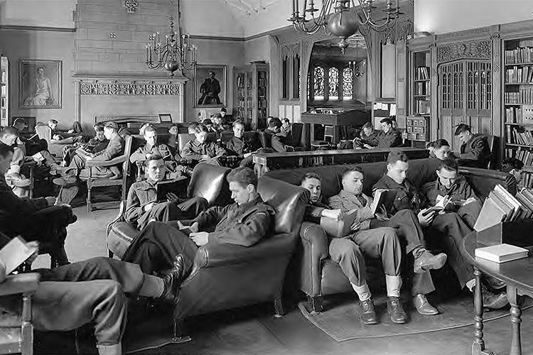 Men in uniform reading books pack every available armchair in an ornate room lined with bookshelves.