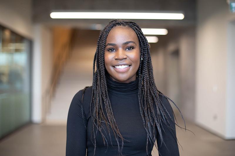 Stephanie Obeta smiles, standing in a brightly lit hallway.