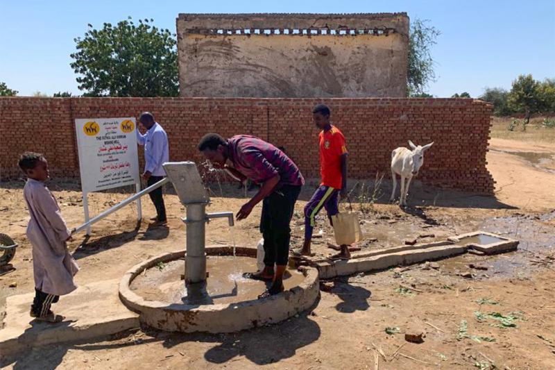 People drink water from a communal pump in a rural area of Darfur, Sudan.