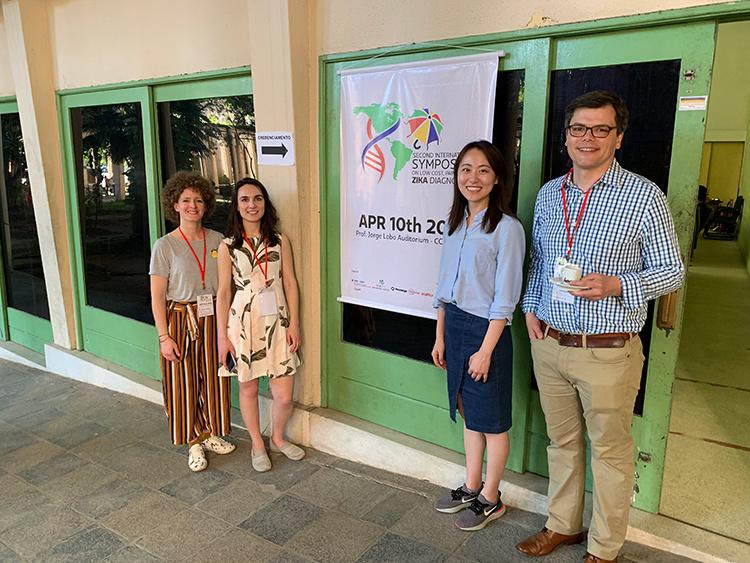Researchers Margot Karlikow, Seray Çiçek, Livia Guo and Keith Pardee stand by a poster for a symposium on Zika studies.