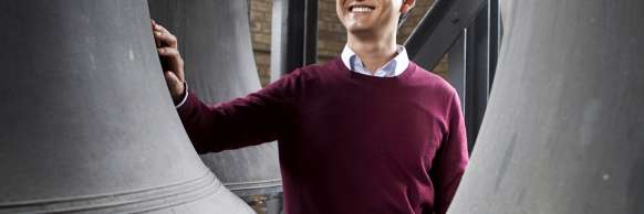 Carillonneur Roy Lee stands between giant bronze bells, smiling. (Image by Michelle Yee Photography.)