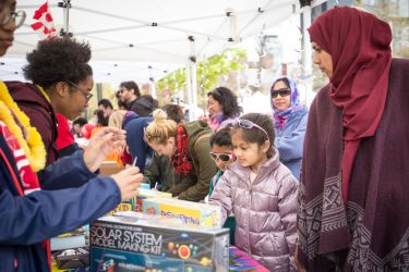 Image shows families visiting science exhibitions staffed by student volunteers.