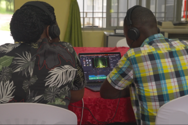 Two men wearing earphones edit a video on a laptop