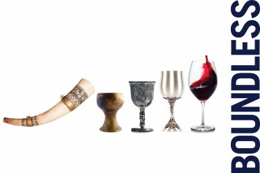 A horn wine glass, wooden goblet, pewter goblet, silver goblet, modern wine glass half-filled with red wine.