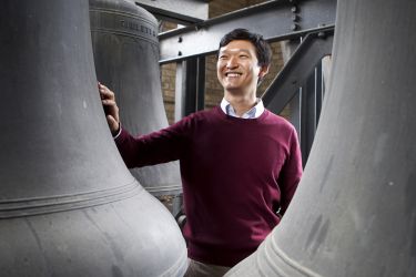 Carillonneur Roy Lee stands between giant bronze bells, smiling. (Image by Michelle Yee Photography.)