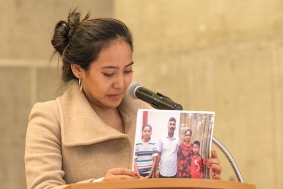 Chemi Lhamo stands at a podium, tearfully holding up a photograph of two parents with their two children. (photo by Don Campbell)