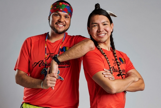Anthony Johnson and James Makokis smiling. Makokis wears a feather and wrapped braids and Johnson wears a headband and necklace.