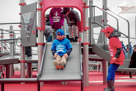 Children play on a slide made of parallel rollers, wearing T-shirts with the Jumpstart logo (photo courtesy of Canadian Tire Jumpstart Charities)