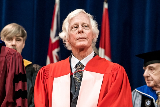 Ted Chamberlain looks serious as he stands on stage at Convocation in academic robes.