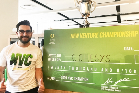 Post-doc Michael Floros smiles while posing next to a giant cheque for $20,000.