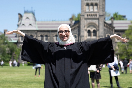 Noura AliJizawi smiles and holds out her hands as she stands on Front Campus in her graduation gown.