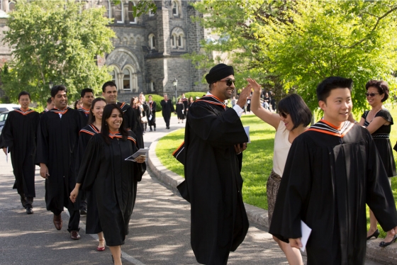A student in academic robes steps out of line to high five a friend as graduates walk along King's College Circle to Convocation Hall.