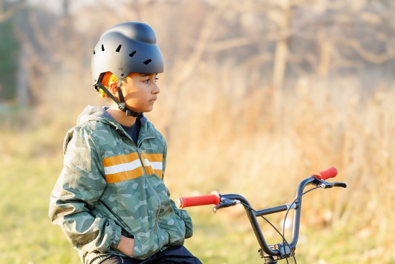 A boy stands beside his bike wearing a helmet that allows for his head covering