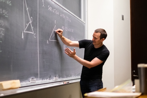 Zack Wolske gestures as he writes a geometry problem on a chalkboard.