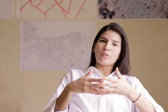 Gabriela Luna Vélez gestures while talking in front of a display of architectural drawings.