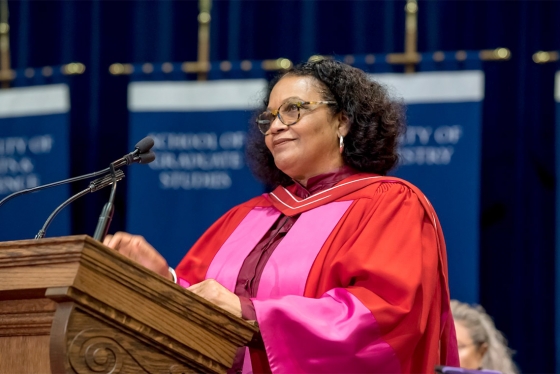 Lorna Goodison smiles while standing an a podium and wearing academic robes.