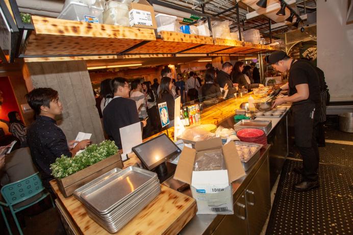 view from behind the sushi serving station, chef prepares food while alumni watch