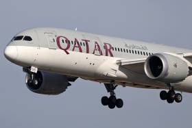 A jumbo jet with wheels down flies low. Letters on the side of the plane read: Qatar.