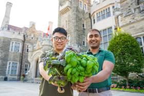 Leo and Adnan holding basil plants in front of the Casa Loma building