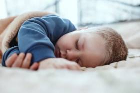 A baby in a blue sweatshirt sleeping on its side
