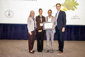 Dr. Vivian Rambihar accepts his award on stage from three other people, Carl Mitchell's wife Margaret Shaw, daughter Nancy Mitchell and UTAA President Corwin Cambray.