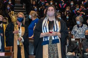 The audience in Convocation Hall stands as Lindsey Fechtig walks down an aisle holding an eagle feather.