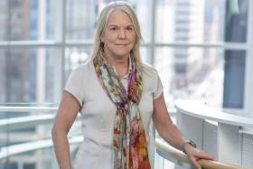 A portrait of Stinton wearing a white t-shirt with a floral scarf tied elegantly around her neck