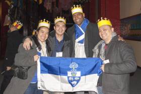 4 alumni standing together smiling holding a uoft flag