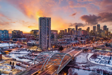 Image of a sunset, with a skyscraper and a bridge with snow on the ground. 
