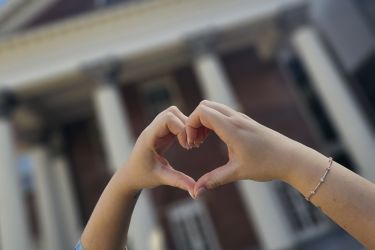 Two hands forming a heart with Flavelle House in the background