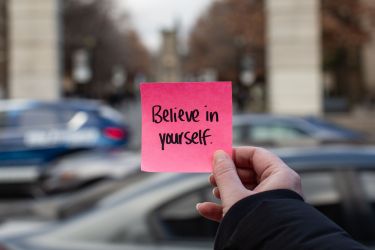 Person holding sticky note that says "Believe in Yourself.