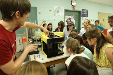 Elementary students looking at a 3D printer in a summer camp